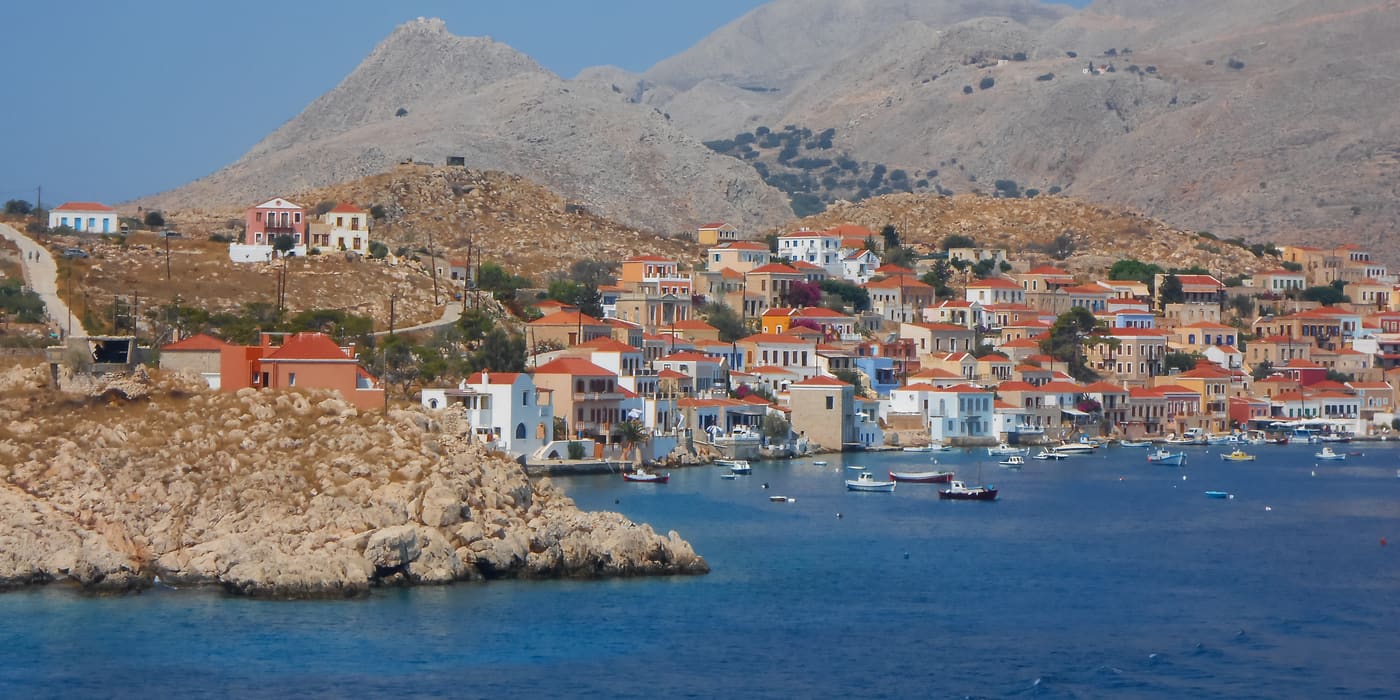 Colourful houses of Emborio harbour on Chalki below bare mountains