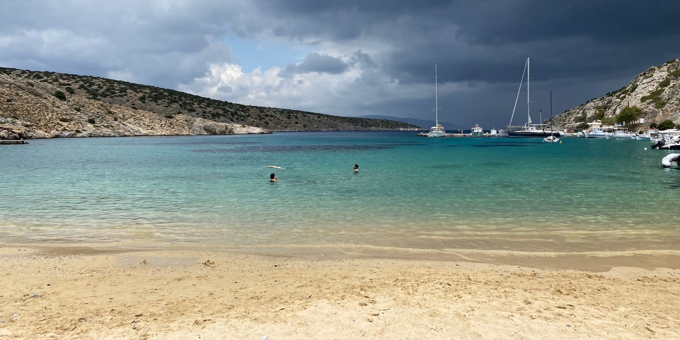 Sandy beach and anchored sailboats under storm clouds on Iraklia