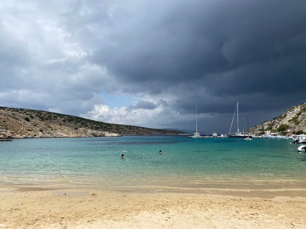 Sandy beach and anchored sailboats under storm clouds on Iraklia